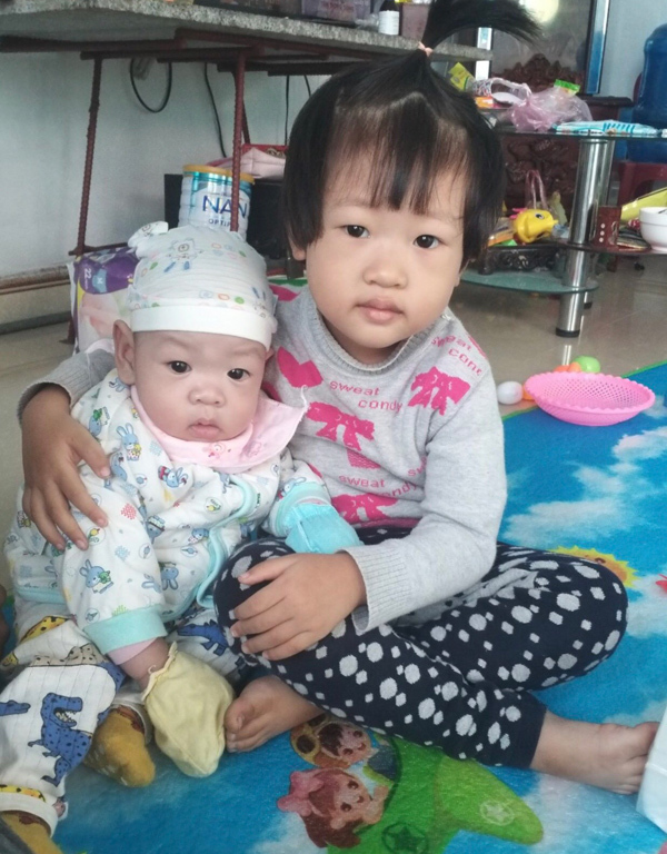 Bình An bụ bẫm ngồi cạnh chị gái. Cậu bé kháu khỉnh đã đòi tập đi dù mới 8 tháng