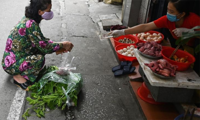 Người phụ nữ mua hàng và chủ quán đều đeo khẩu trang, thực hiện giãn cách xã hội. Ảnh: AFP.