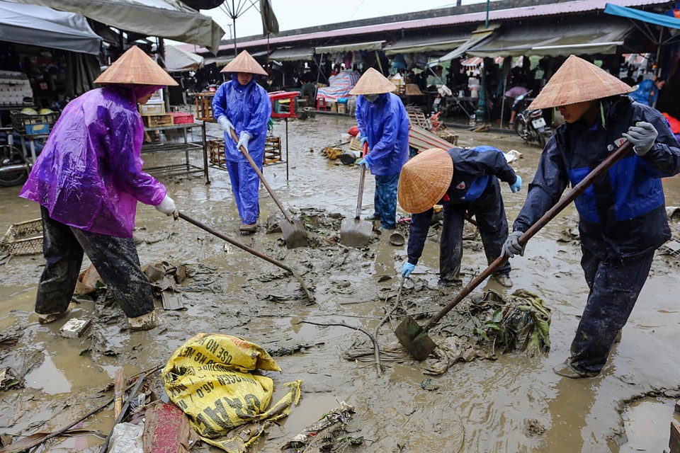 Tại chợ Hội An, nhóm công nhân môi trường dùng xẻng thu dọn rác thải, bùn đất đọng lại sau lũ. Ảnh: Đắc Thành.