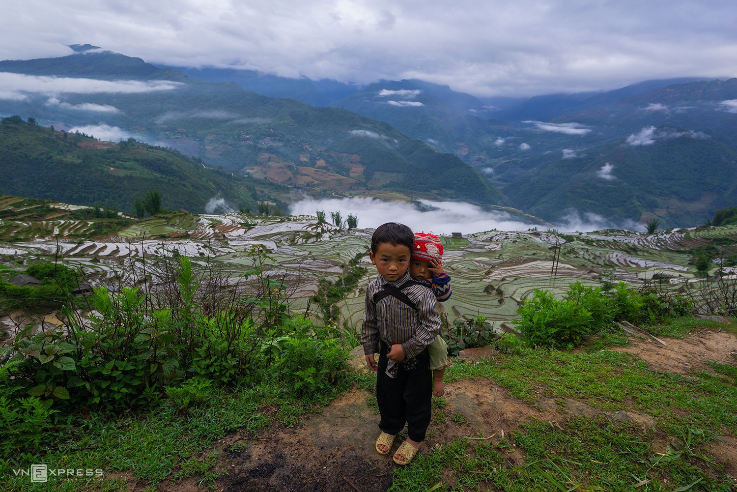 A boy carries his younger brother as their parents work on the rice terraces of Ngai Thau.

