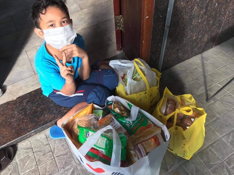 A family member of Moana Tranh, a Filipina living in District 9, poses for a photo next to food packages sent by CJ Van Burren. Photo courtesy of Moana Tranh.