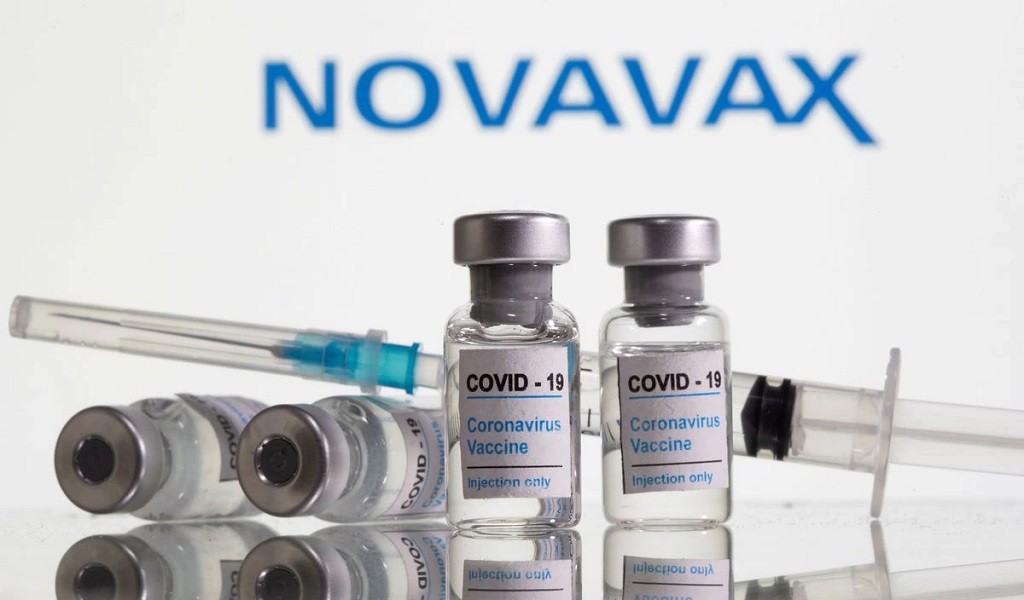 Các lọ dán nhãn vaccine ngừa Covid-19 và ống tiêm được nhìn thấy phía trước logo Novavax. (Ảnh: Reuters).