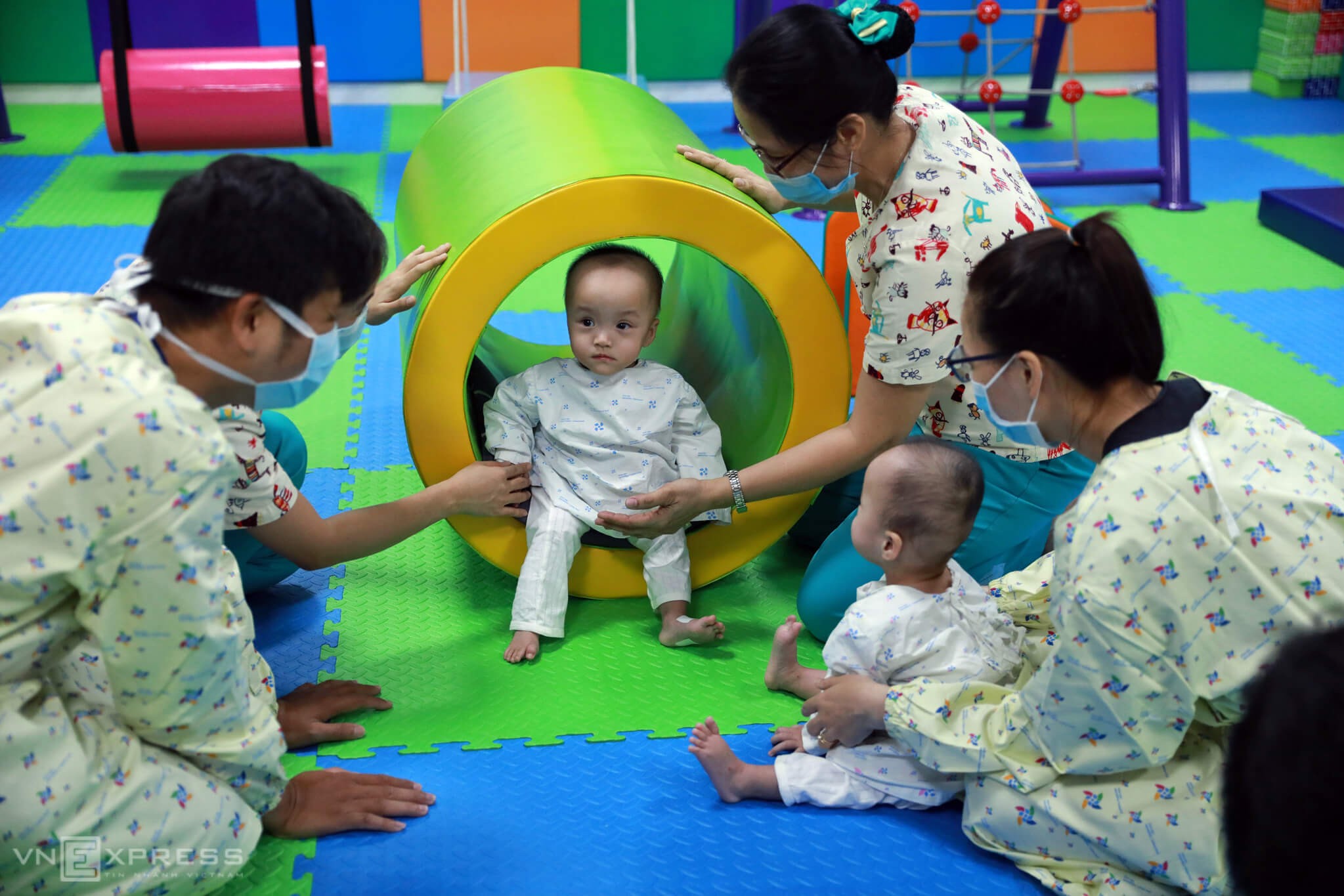 Mỗi bài tập, hai bé được các chuyên viên bố trí trong các không gian nhiều màu sắc và vật dụng khác nhau.

Kỹ thuật viên Đỗ Thị Bích Thuận, Trưởng khoa Phục hồi chức năng và bố mẹ hai bé Trúc Nhi, Diệu Nhi, cho hai chị em thực hiện bài tập phát triển chức năng vận động, giúp bé kích thích cảm giác bản thể, tiền đình và phát triển thăng bằng ngồi.