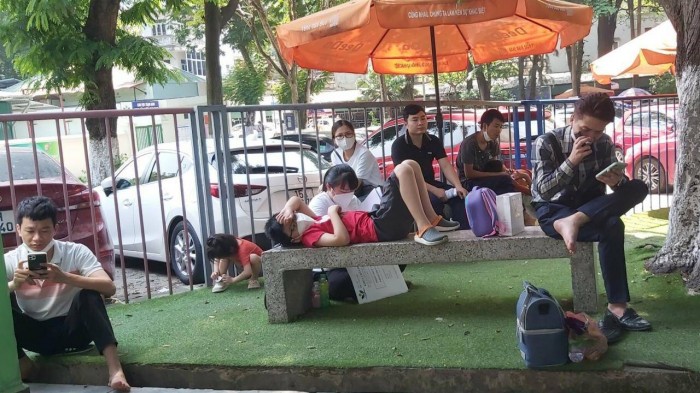 Một bệnh nhi mệt mỏi nằm dài trên ghế băng, dưới tán cây tránh nắng đợi đến lượt khám