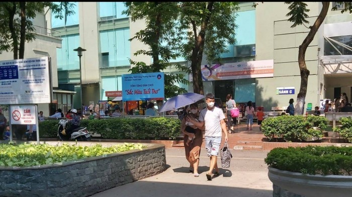 Một ông bố giương ô che nắng cho vợ và con trong sân bệnh viện
